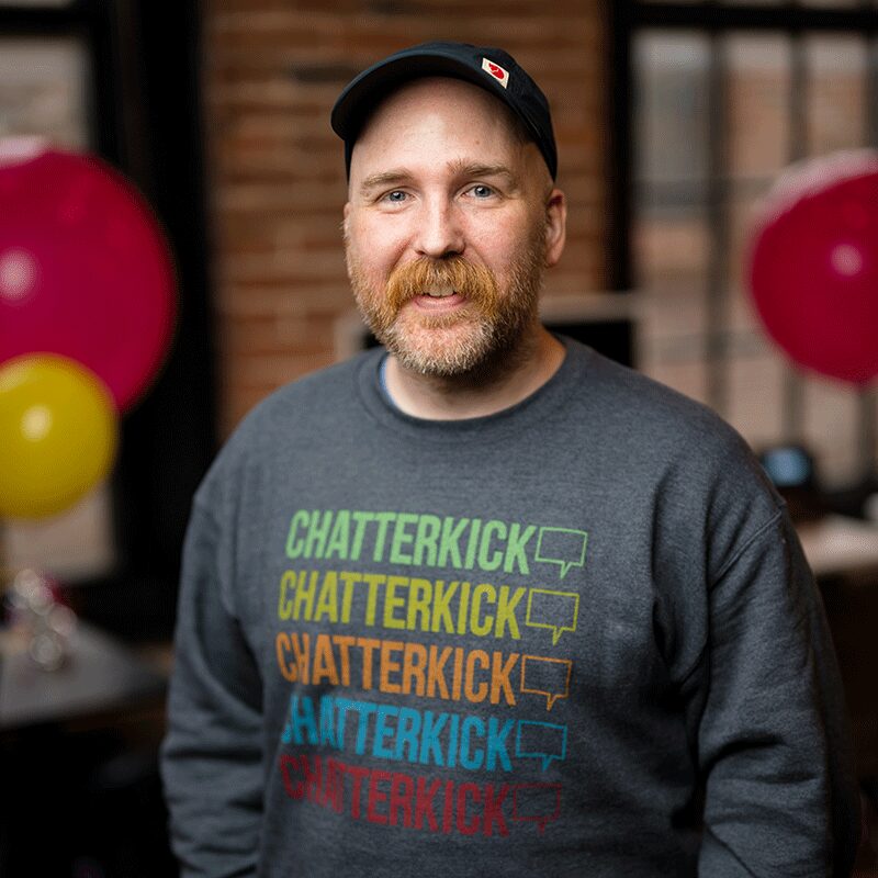 Austin posing with a gray crewneck sweater with Chatterkick logos on it