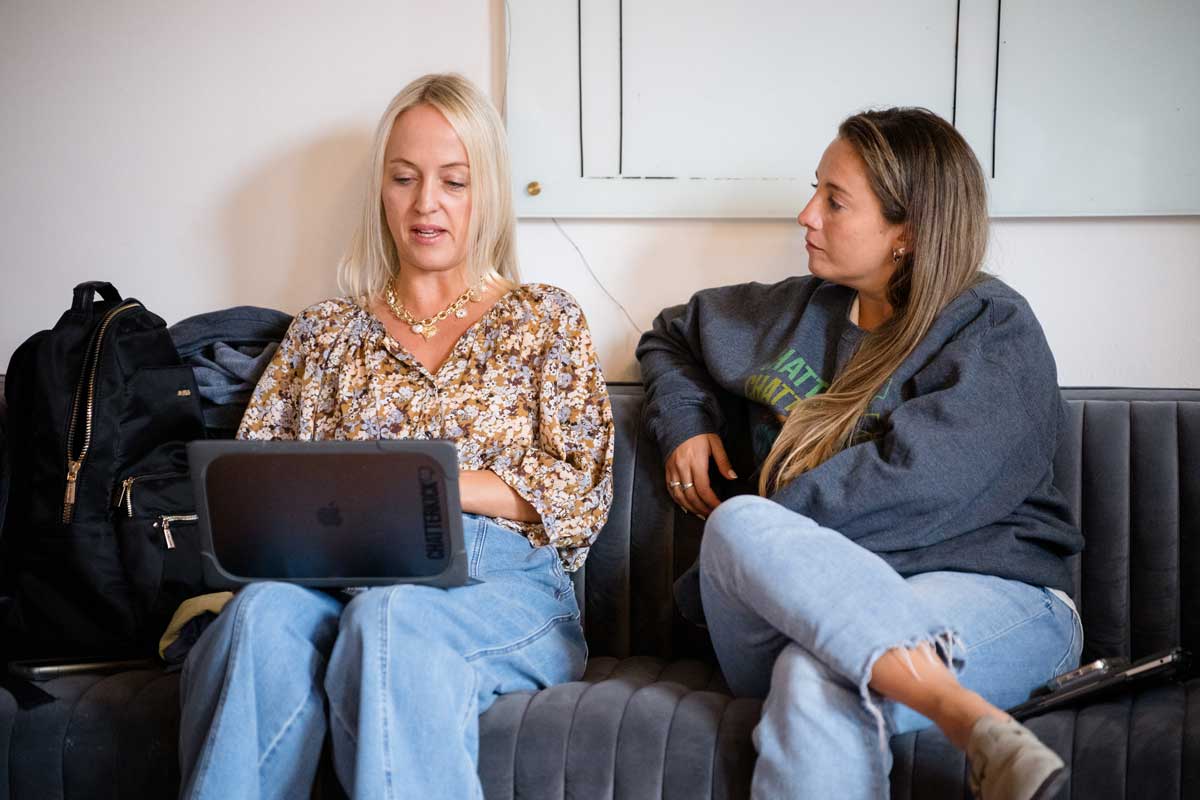 Mary and Aileen talking while sitting on a couch with a laptop